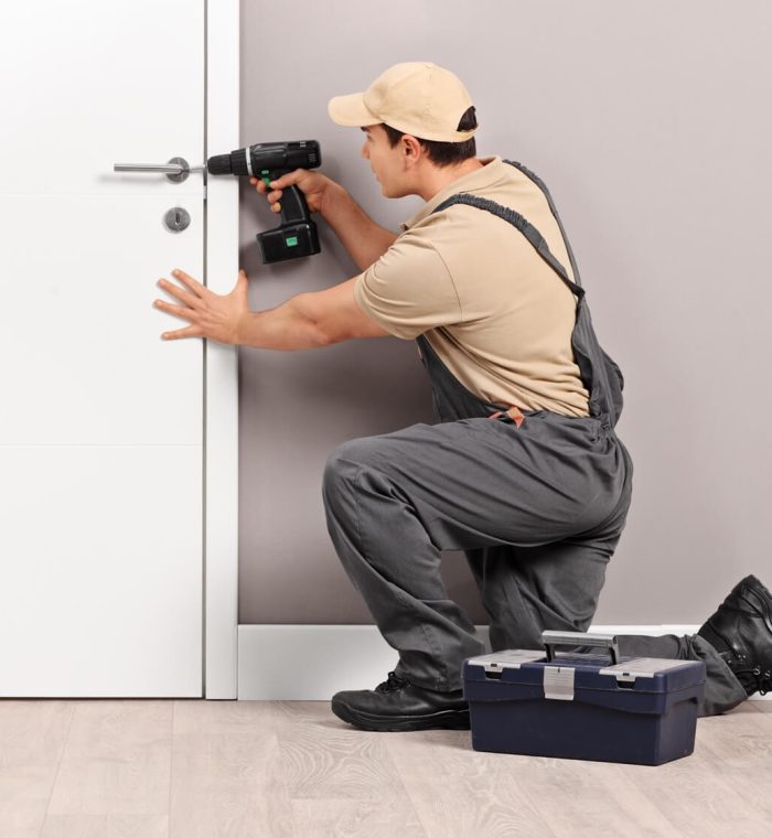 Emergency locksmith technician using a power drill on a door lock, with a toolbox nearby, demonstrating urgent lock repair services.