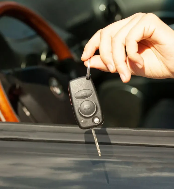 Hand holding an automotive key fob with a key, representing automotive locksmith services for vehicle access and key replacement.